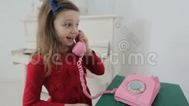 家里有粉色复古手机的有趣小女孩。她手里拿着粉色复古手机和妈妈聊天